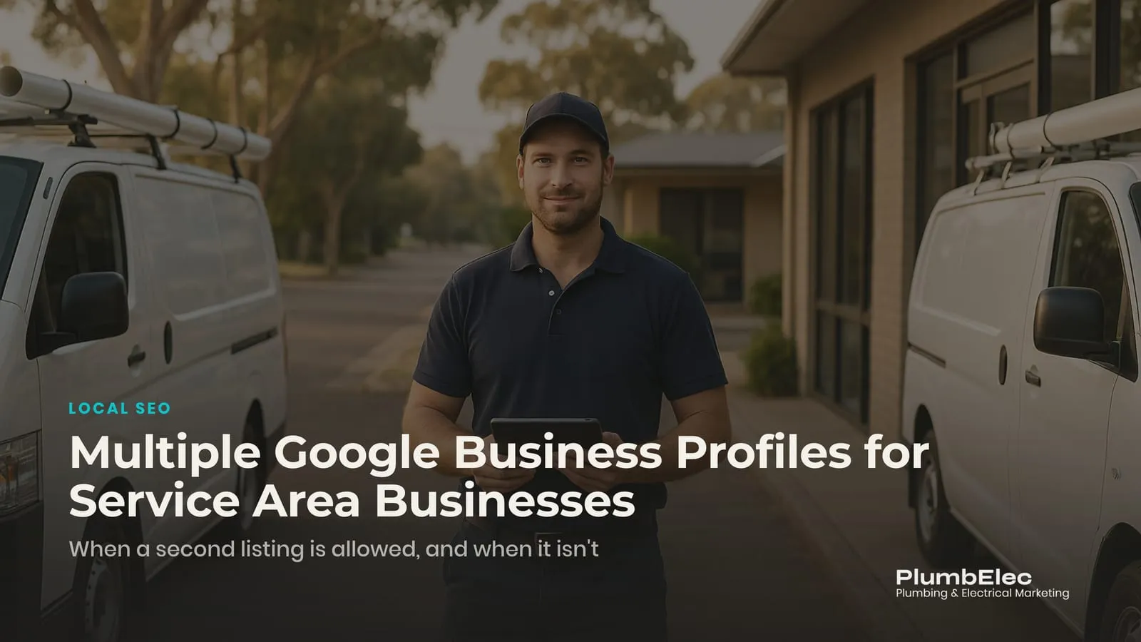 Plumber with a tablet standing between two work vans outside a small suburban office